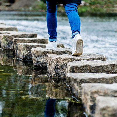 Eine Frau, die auf Trittsteine einen Fluss überquert.