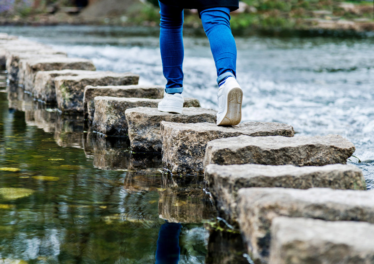 Eine Frau, die auf Trittsteine einen Fluss überquert.