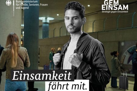 Ein junger Mann steht alleine am Bahnhof. Auf dem Bild steht "Einsamkeit fährt mit".