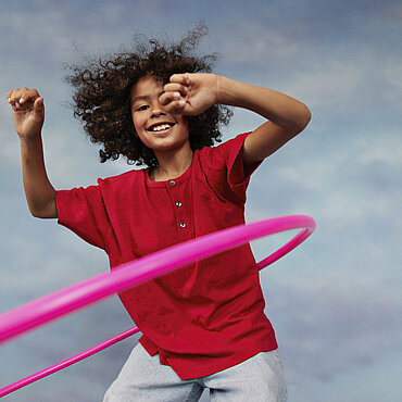 Eine Junge in rotem T-Shirt lässt einen Hula Hoop Ring kreisen.