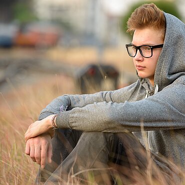 Junge sitzt auf Feld. Er guckt nachdenklich und trägt einen Kapuzenpullover.