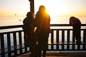 Eine Frau und zwei Kinder blicken dem Sonnenuntergang entgegen.
