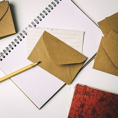 Mehrere Briefumschläge und ein Schreibblock mit einem Bleistift auf weißer Tischoberfläche