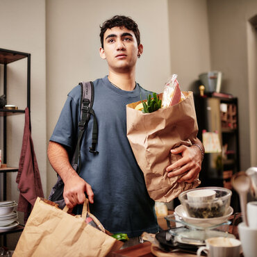 Ein junger Mensch steht in der Küche und hält Einkaufstüten.