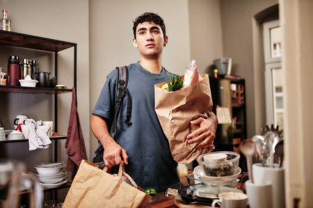 Ein junger Mensch steht in der Küche und hält Einkaufstüten.